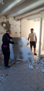femme et homme détruisant un mur de placoplâtres dans une pièce à demi éclairée