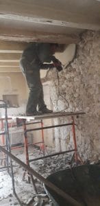 homme en côte de travail piquant les murs avec un marteau piqueur sur un échafaudage