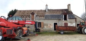 vieille toiture faite de latte en démolition, avec un élévateur à côté et une remorque de tracteur