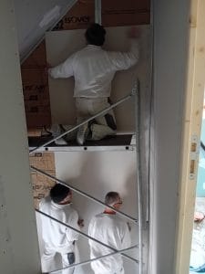 trois plaquistes sur un échafaudage qui montent une cloison dans une cage d'escalier