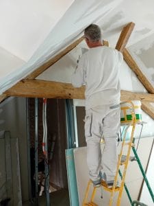 homme de dos monté sur un escabeau qui fait des bandes de placoplâtres entre les poutres apparentes