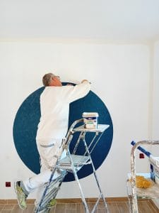 peintre-en train-de-découper-du-papier-peint-bleu-en-rond-sur-un-mur-beige