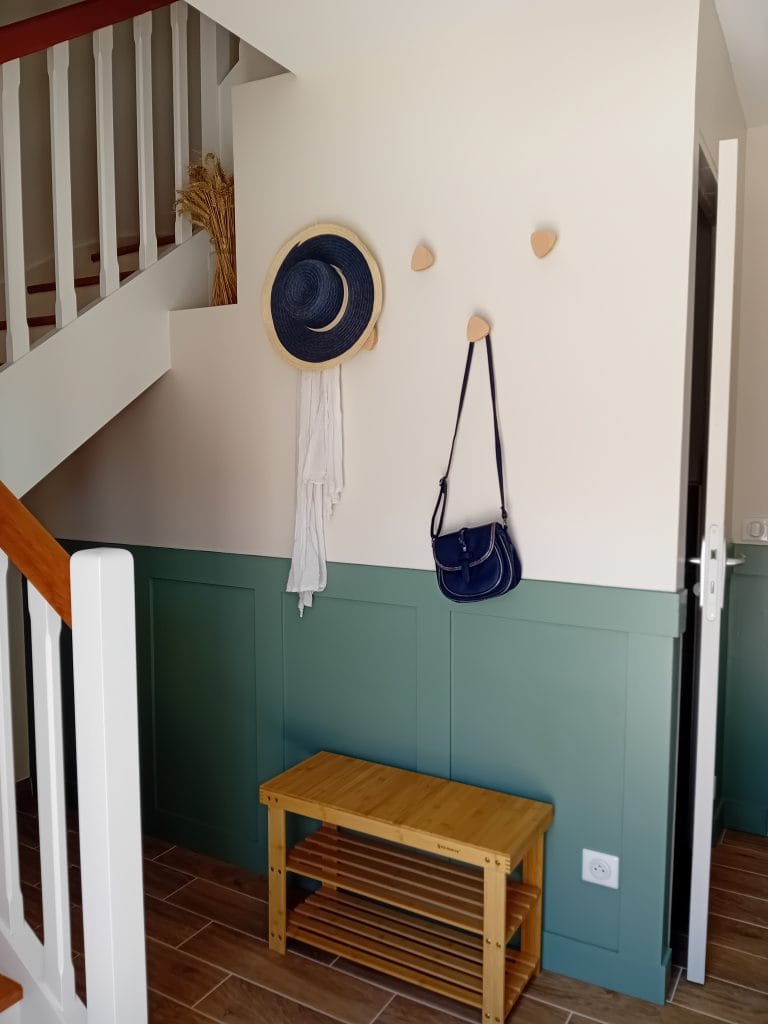 rampe-d'escalier-blanc-et-bois-avec-patère-en-bois sur mur beige-et-sous-bassement-vert où se trouve un range-chaussures-en-bambou