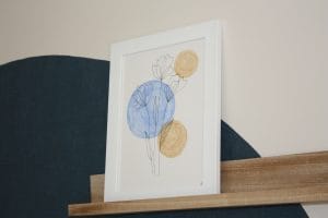 cadre-blanc-avec-dessin-de-fleur-bleu-et-beige-sur-étagère-en-bois