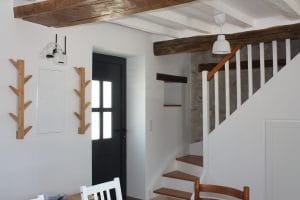 escalier-blanc-et-bois-avec-porte-manteau-à-coté-dela-porte-d'entrée-poutre-blanche-au-plafond