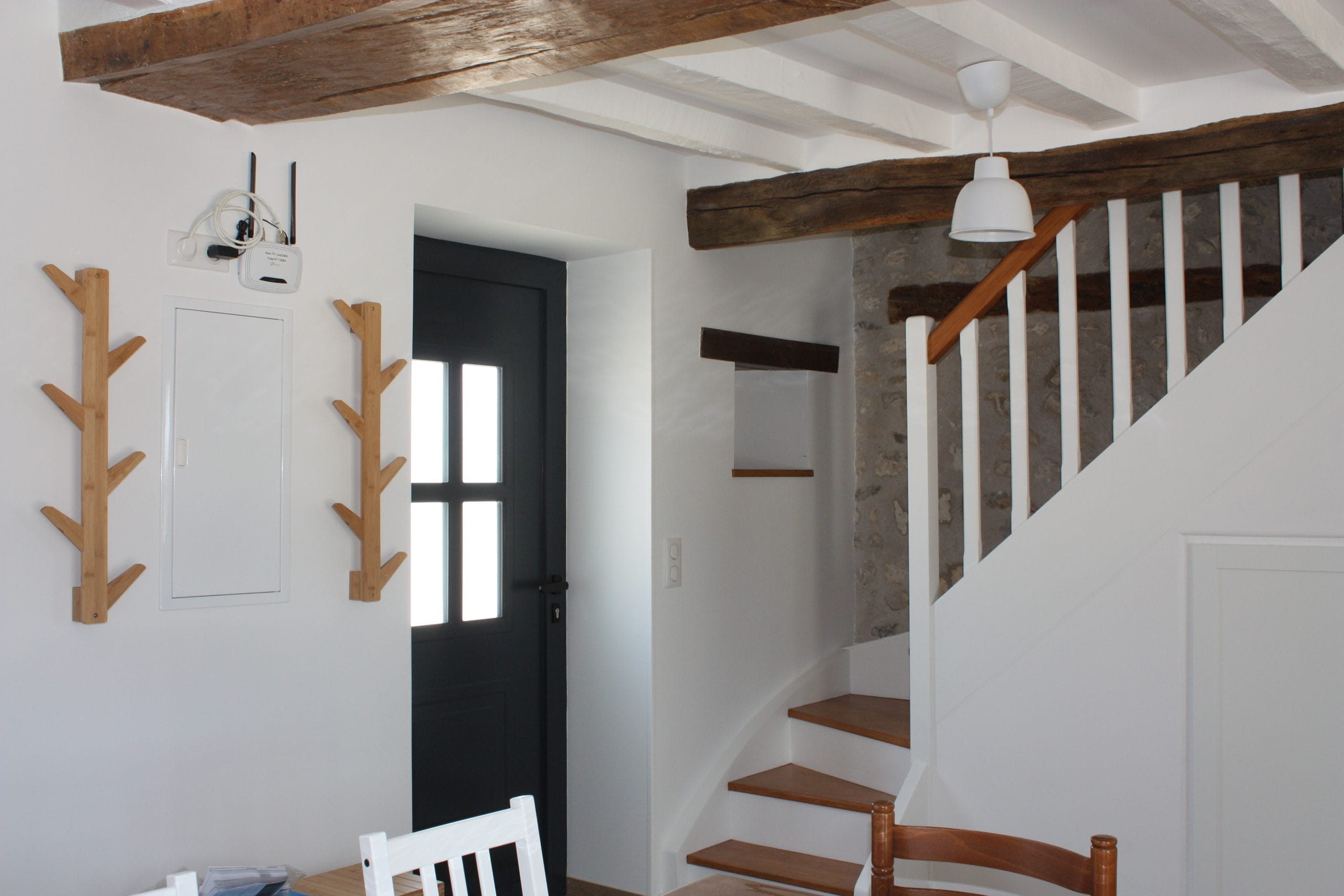 escalier-blanc-et-bois-avec-porte-manteau-à-coté-dela-porte-d'entrée-poutre-blanche-au-plafond