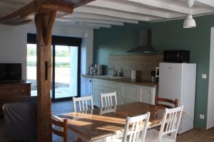 meuble-de-cuisine-blanc-avec-plan-de-travail-en-bois-poutre-blanches-au-plafond et mur peint en vert. table-en-bois-avec-chaises et baie-vitrée en arrière-plan