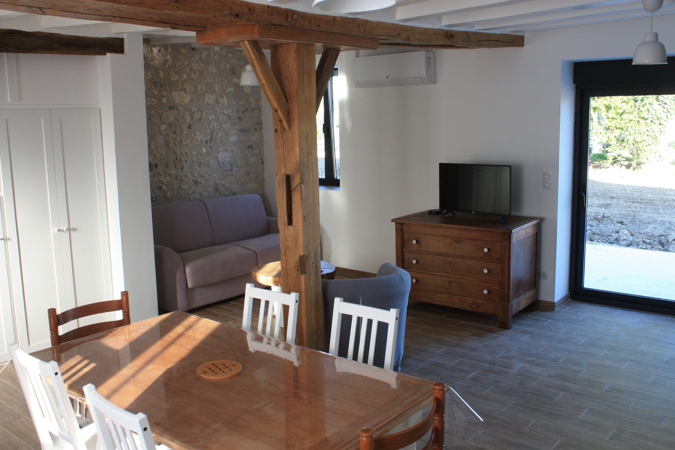 table et des chaises de salle à manger-en-bois-au-premier-plan-canapé-et-meuble-télé-au-second-plan. sol en carrelage imitation parquet