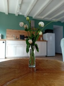 Petit bouquet de lisianthus blancs posé sur une table basse en bois, on distingue la cuisine blanche et bois en arrière plan