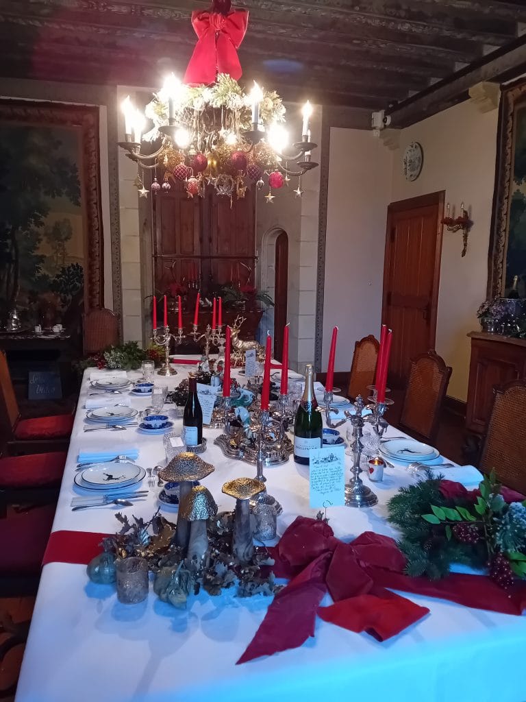 Table de Noël décorée avec belle vaisselle et bougies rouges, un grand lustre est situé au dessus décoré avec un gros nœud rouge