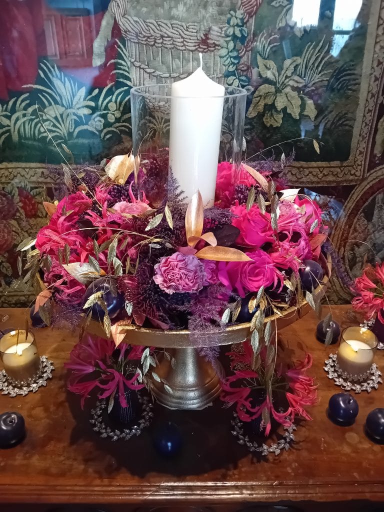 Décoration de fleurs séchées de couleur rose et or posée sur une coupe avec une bougie blanche au centre