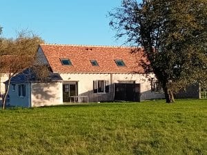 vue arrière de la maison avec terrasse et séparation , toit en tuiles avec velux . grande étendue de pelouse au premier plan