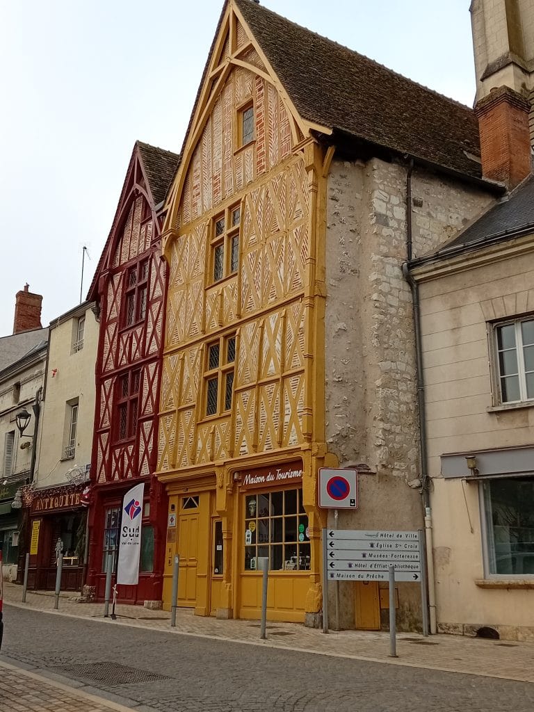 deux maisons à pans de bois l'une à façade jaune et l'autre rouge avec une ruelle pavée juste devant.