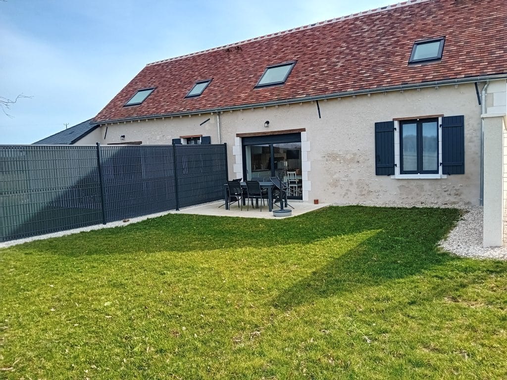 terrasse en béton entourée de pelouse avec 6 chaises et une table de salon de jardin avec vue sur arrière de la maisson