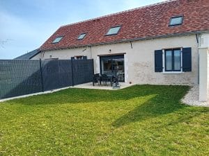 terrasse en béton entourée de pelouse avec 6 chaises et une table de salon de jardin avec vue sur arrière de la maisson