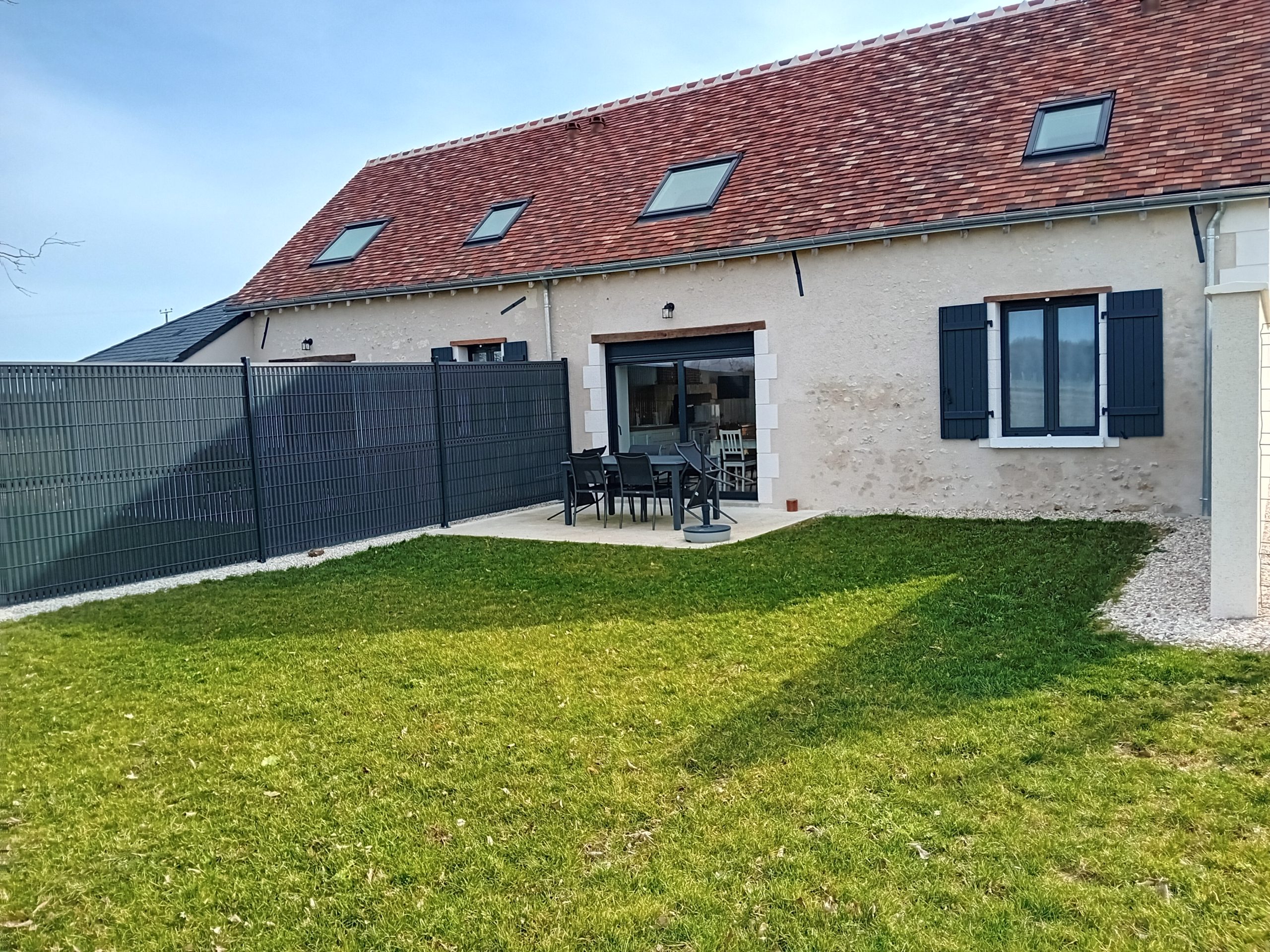 terrasse en béton entourée de pelouse avec 6 chaises et une table de salon de jardin avec vue sur arrière de la maisson
