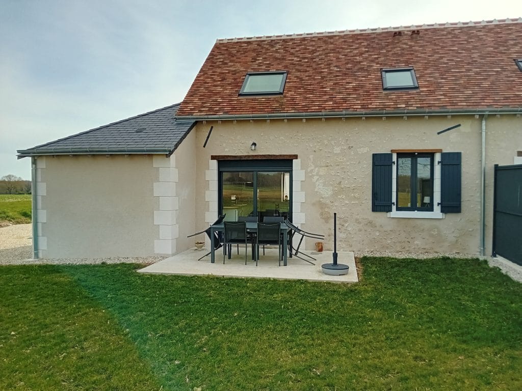 terrasse en béton entourée de pelouse avec 6 chaises et une table de salon de jardin avec vue sur arrière de la maison