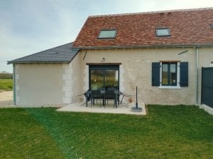terrasse en béton entourée de pelouse avec 6 chaises et une table de salon de jardin avec vue sur arrière de la maison