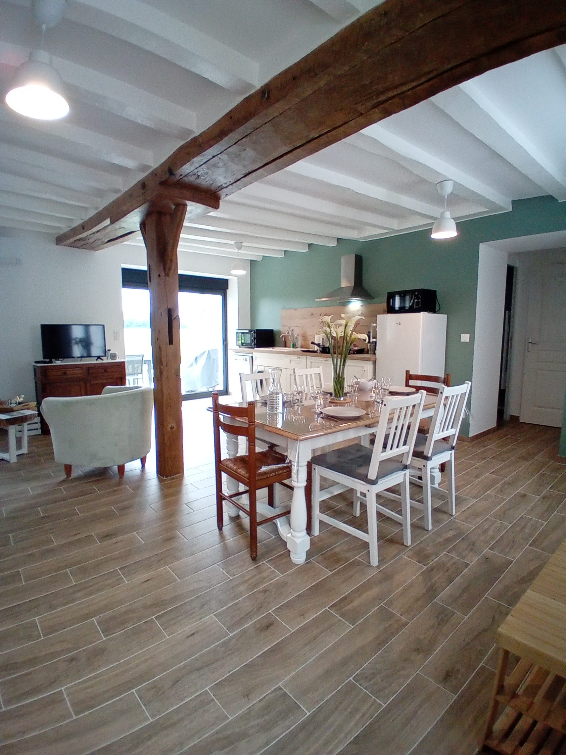 pièce avec table et chaises blanches carrelage imitation bois en arrière plan cuisine blanche avec mur vert