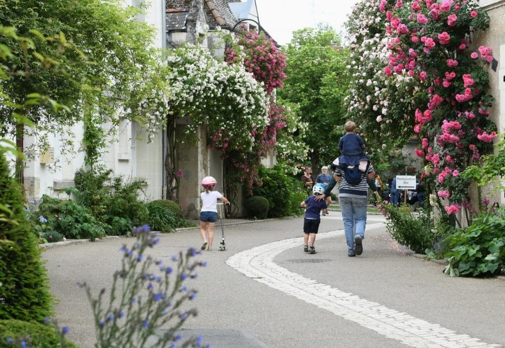 Village jardin de Chédigny avec rosier blanc et rosier rose, une famille marchant sur la route pavée