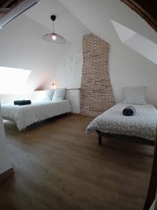 chambre avec 1 lit double et 1 lit simple, conduit de cheminée en brique apparent et parquet au sol