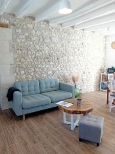 salon avec canapé, table basse et pouf avec pierres apparentes en fond