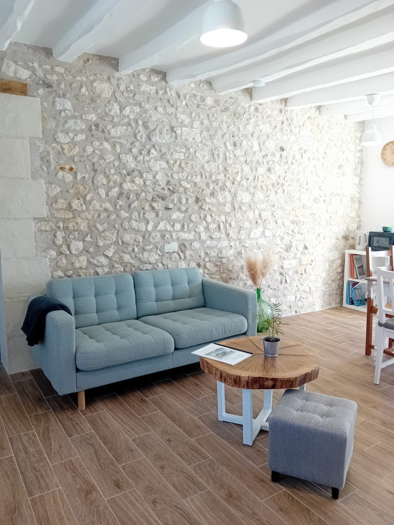 salon avec canapé, table basse et pouf avec pierres apparentes en fond